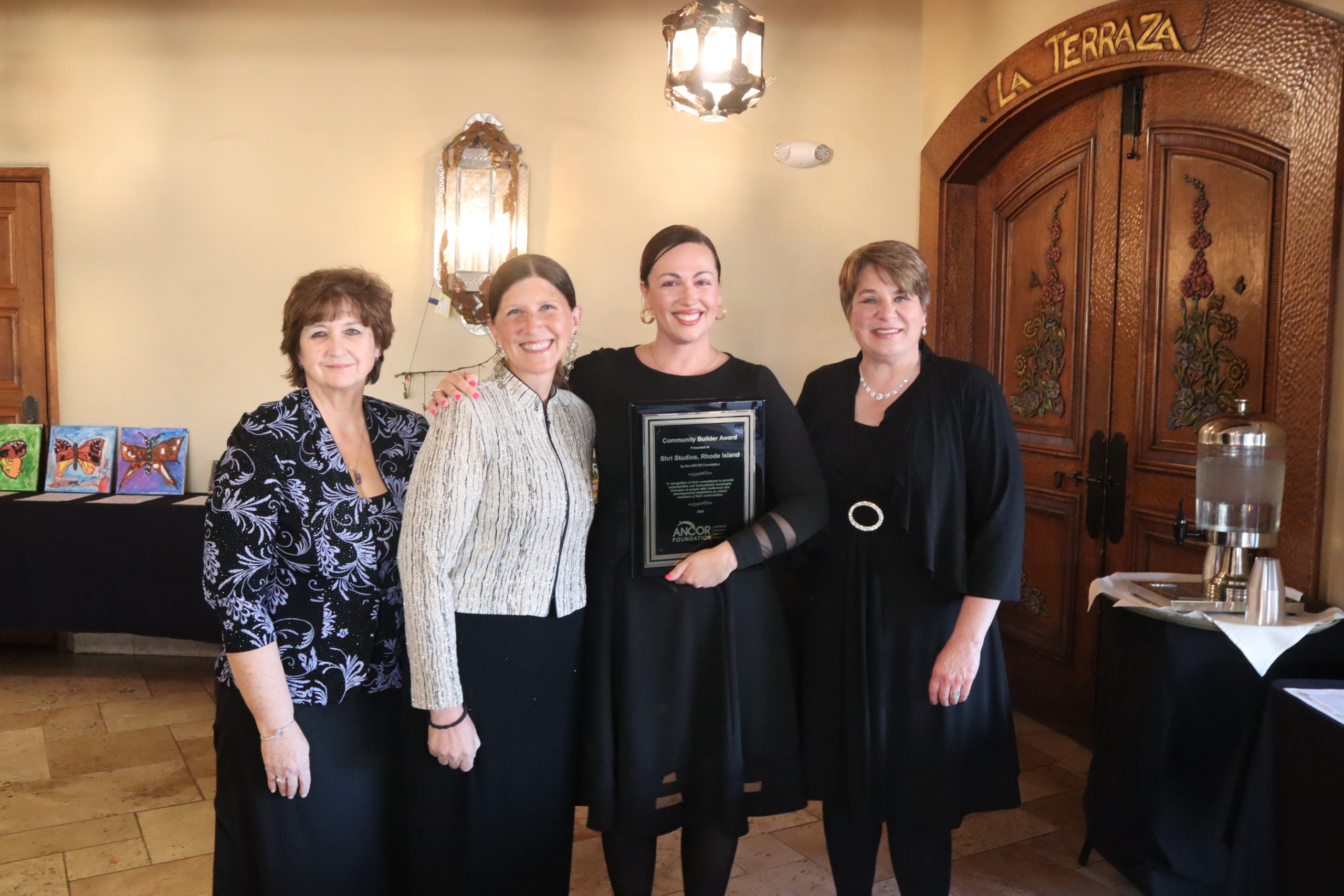 A woman in a black dress posing with three other women as they present her with the 2024 Community Builder Award