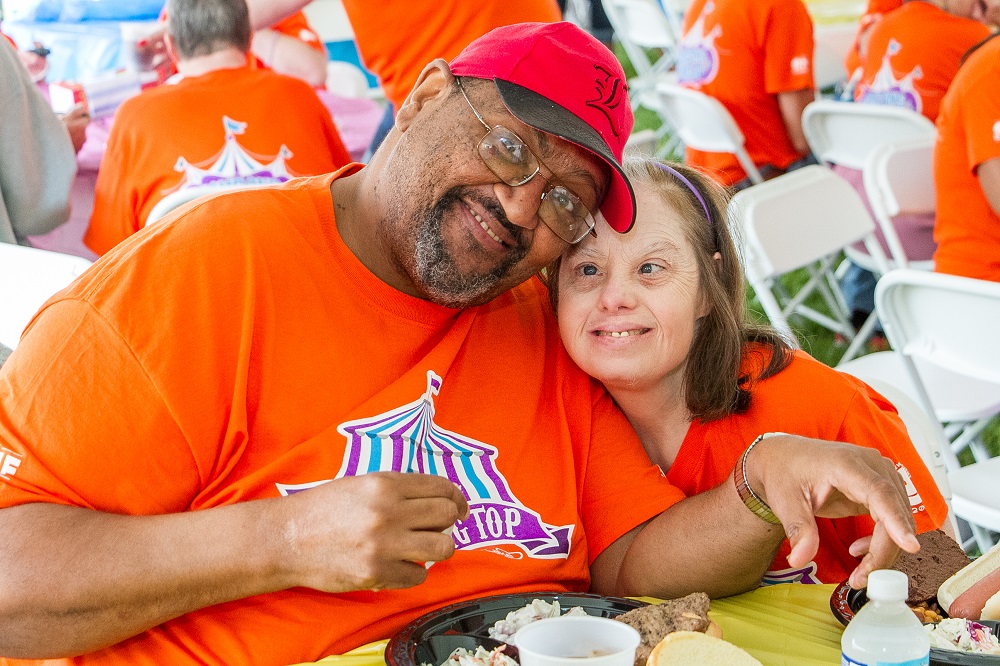 A man and a woman supported by Cedar Lake posing together at a picnic on a bright, sunny day.