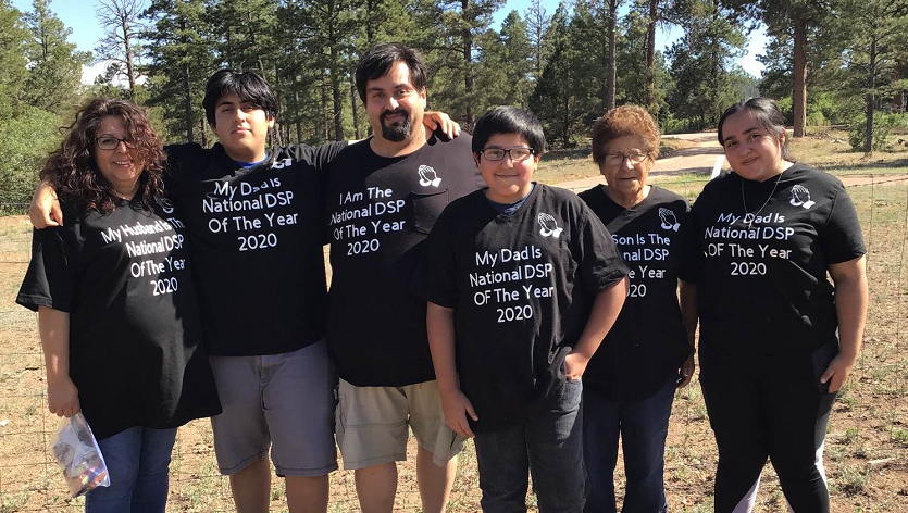 Eligio Velasquez, 2020 DSP of the Year, standing between five family members wearing black shirts celebrating his DSP of the Year award